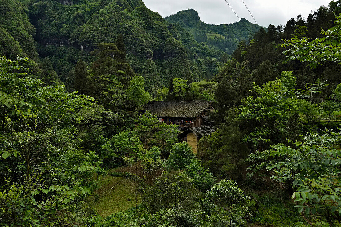 Vegetated limestone mountains tower above a built structure.; Wulong, Chongqing Province, China.