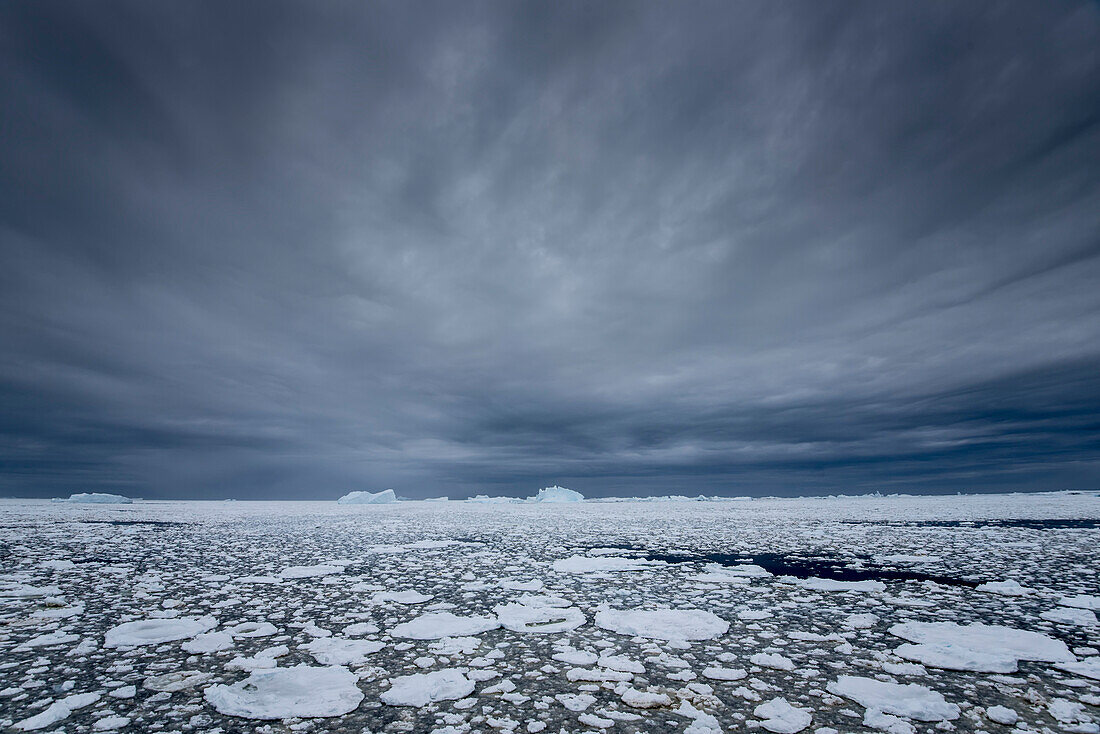 Eisberge in der Penola Strait mit dramatischen grauen Wolken, ein Punkt am südlichsten Ende der meisten Antarktis-Kreuzfahrten; Antarktis