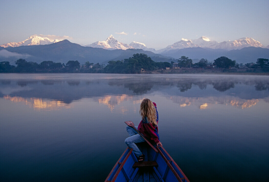 A woman in a rowboat gazes at the Annapurna Range at dawn.; Annapurna Range, Himalaya Mountains, Nepal.