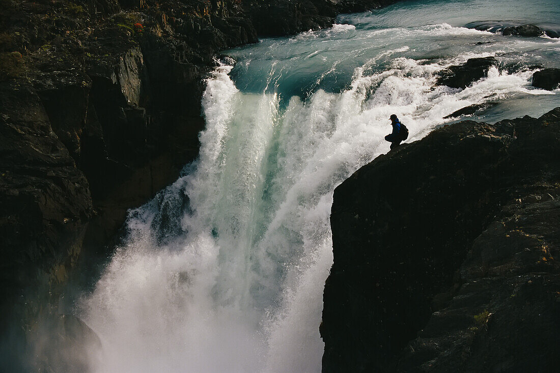 Eine Frau sitzt neben dem Salte Grande Wasserfall in Torres del Paine; Torres del Paine, Chile.
