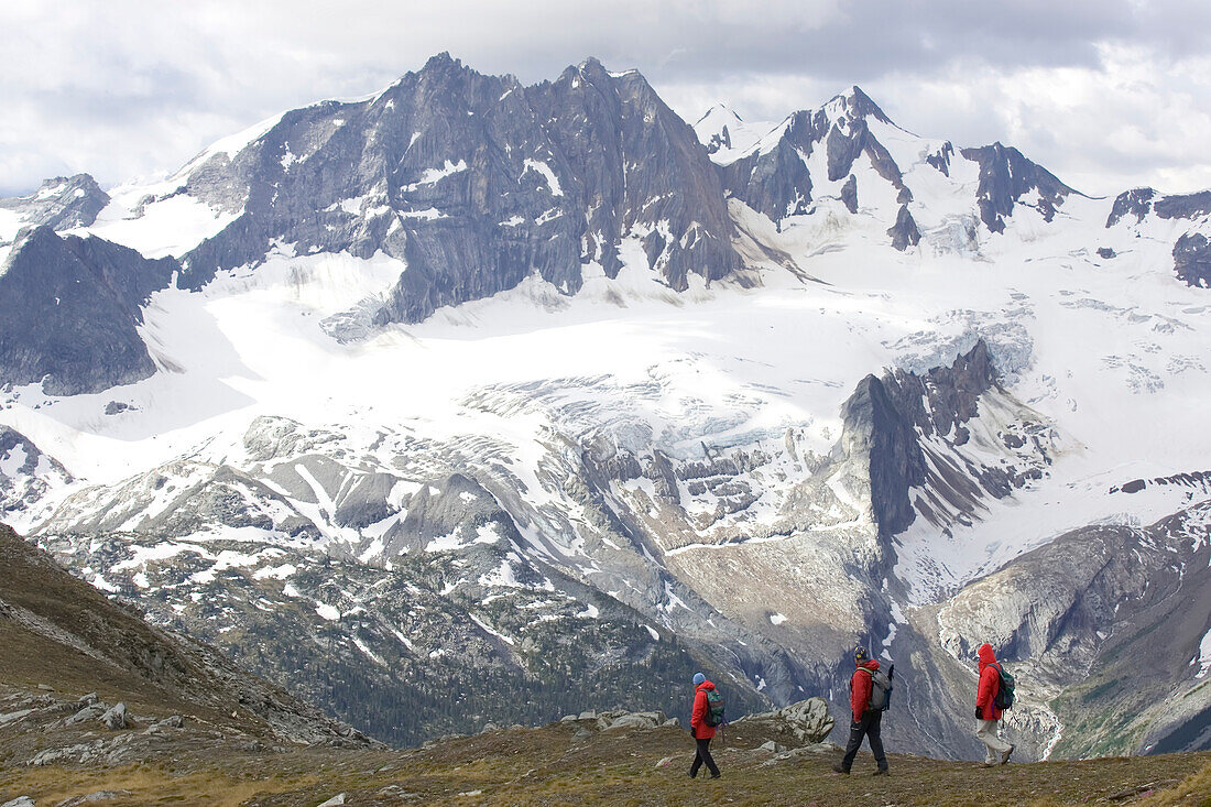 Wanderer auf einer Kammlinie mit schneebedeckten Gipfeln im Hintergrund; Adamants Mountain Range, British Columbia, Kanada