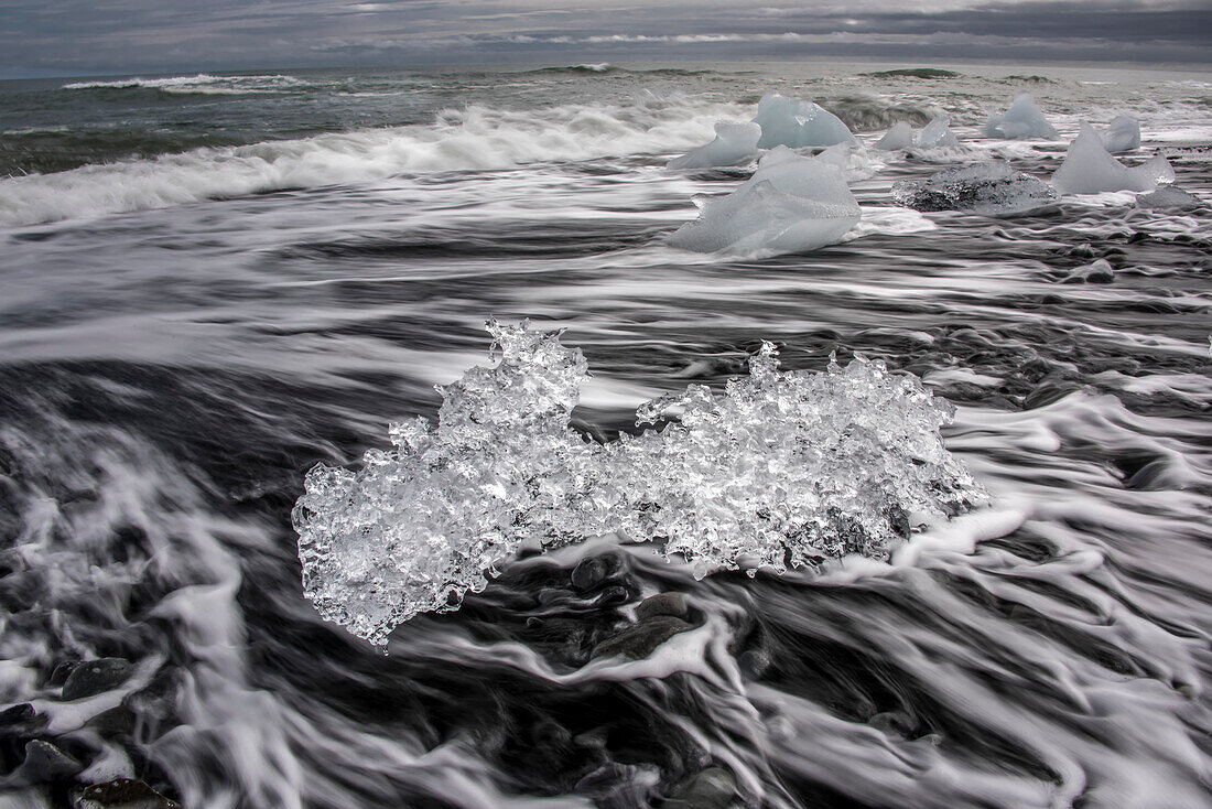 Wellen brechen am schwarzen Sandstrand von Jokulsarlon, der Lagune des Gletscherflusses, wo das Eis des Vatnajokull-Gletschers in die Lagune fällt und dort bleibt, bis es klein genug ist, um ins Meer zu treiben. Der Vatnajokull ist der größte Gletscher in Island; Djupivogur, Südküste, Island