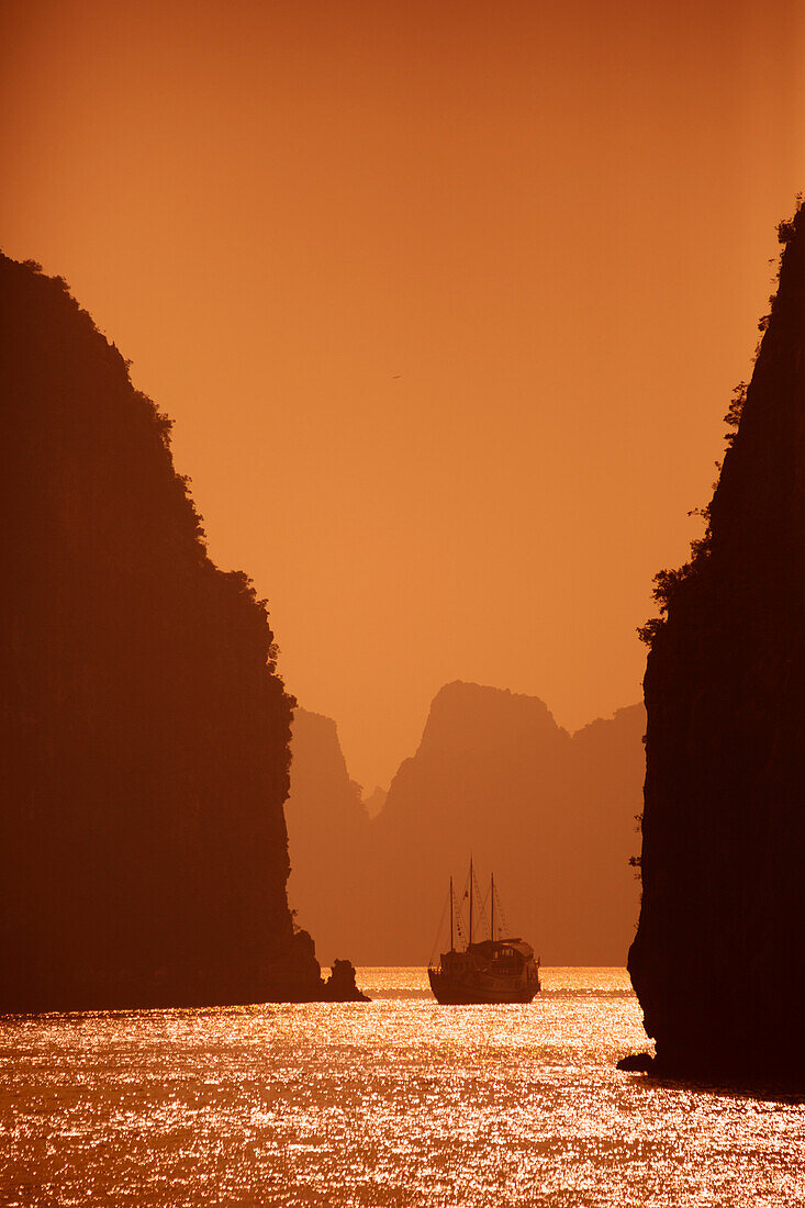Karstformationen und traditionelles vietnamesisches Segelboot (thung chai) bei Sonnenuntergang in der Bai Tu Long Bucht in der Halong Bucht, die zum UNESCO Weltkulturerbe gehört; Halong Bucht, Quang Ninh, Vietnam