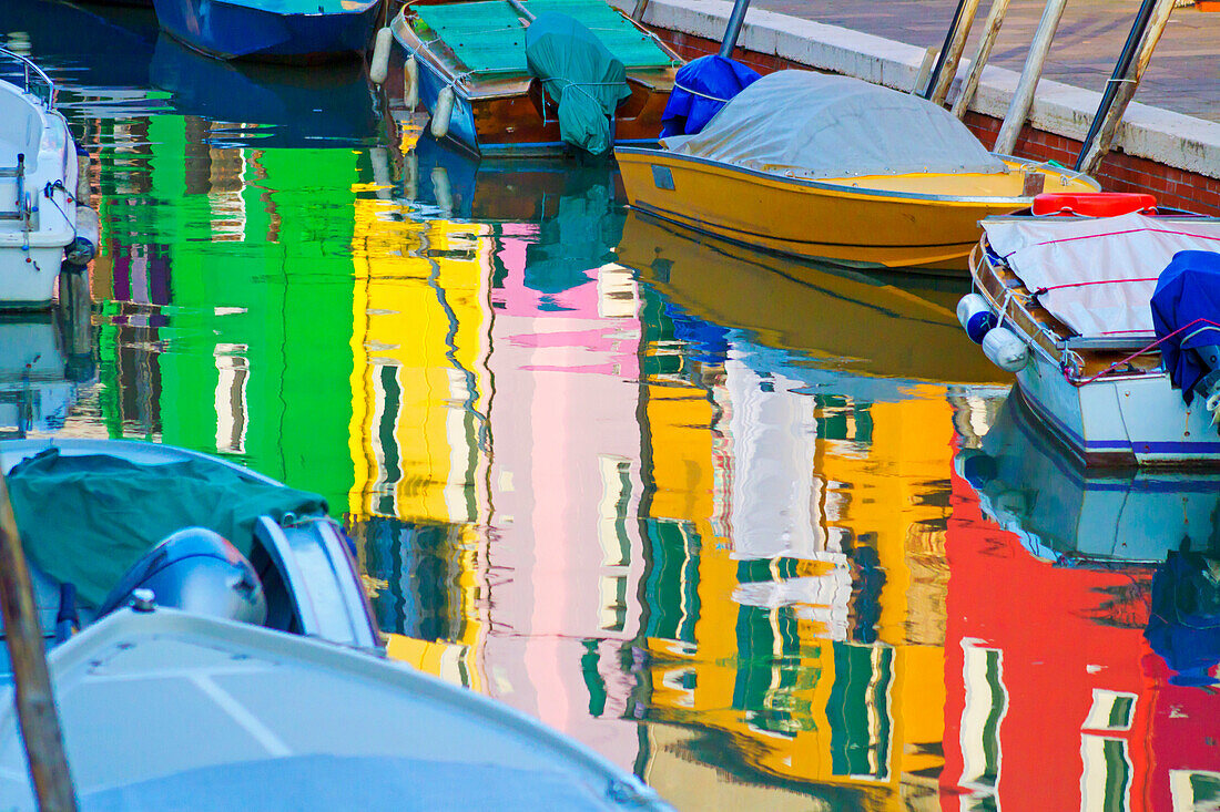 Nahaufnahme von bunten Booten, die am Ufer vertäut sind, und Spiegelungen von bunten Häusern im Wasser in Burano, Italien, einer UNESCO-Weltkulturerbestätte; Insel Burano, Venezianische Lagune, Italien