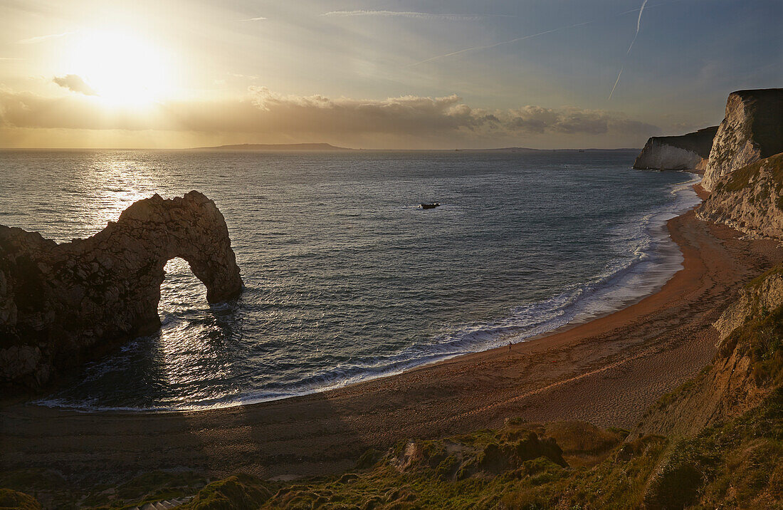 A lone person stands on the Atlantic Ocean shore next to the Durdle Door rock formation on the Jurassic Coast near Lulworth; Dorset, England, Great Britain