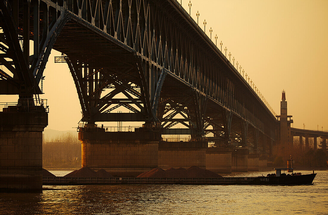 Silhouette eines Schiffes, das unter der Jangtse-Brücke hindurchfährt und den Fluss Jangtse in der Dämmerung überquert; Nanjing, Provinz Jiangsu, China