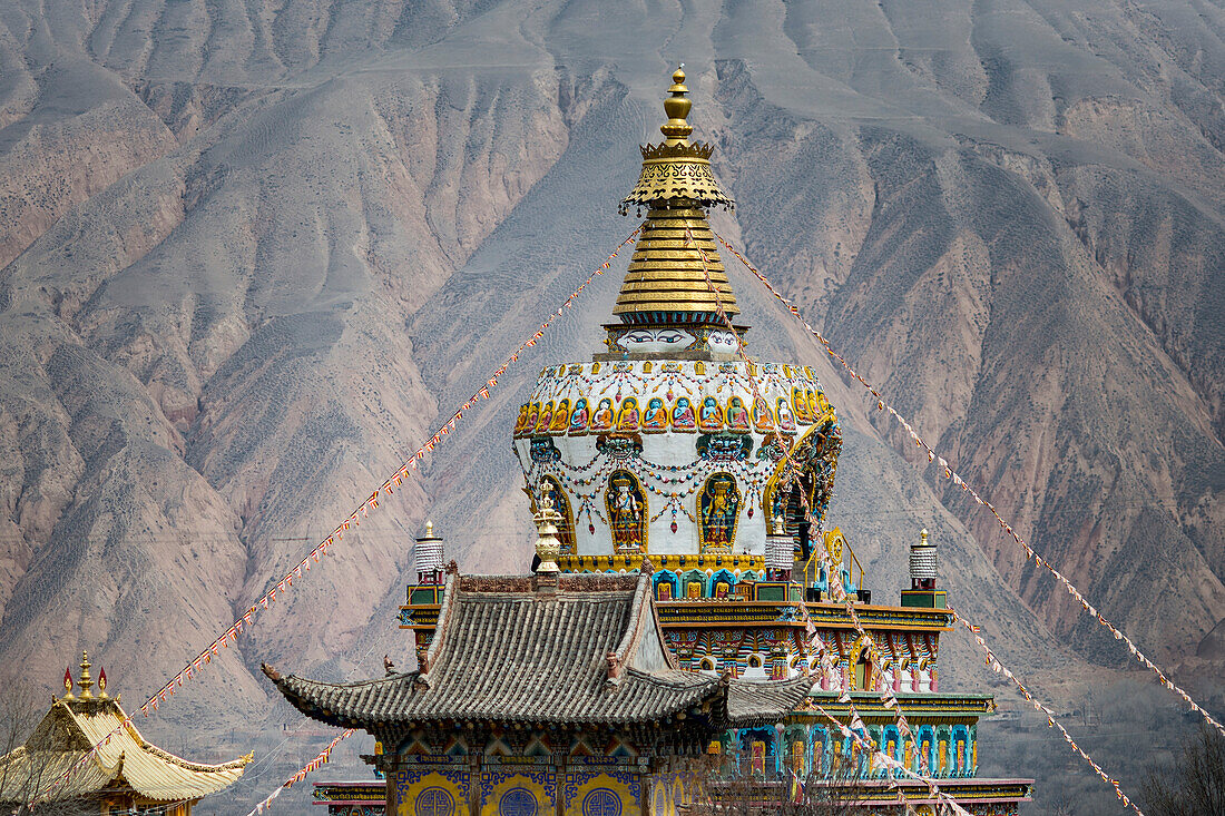 The rooftop of a Buddhist Temple at the Labrang Monastery with the mountain ridges of the Himalayas in the background; Labrang, Amdo, Tibet