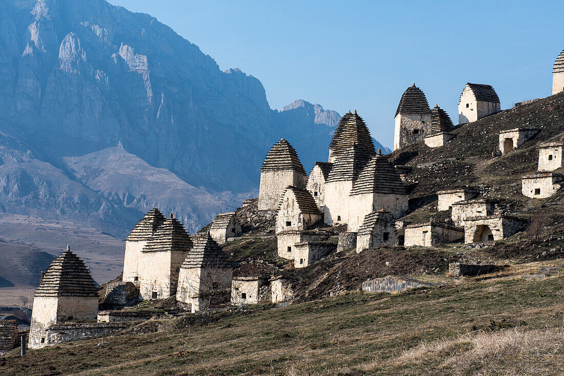 Verlassenes Dorf mit traditionellen Kegeldachhütten am Berghang in Inguschetien mit zerklüfteten Bergkämmen im Hintergrund; Republik Inguschetien, Russland