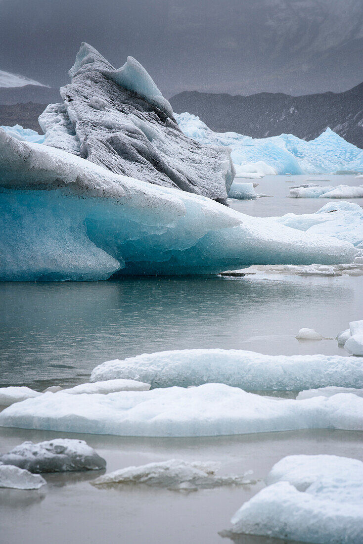 Close-up view of snowfall over icebergs along the shore of Jokulsarlon glacial lagoon; Vatnajokull National Park, Iceland