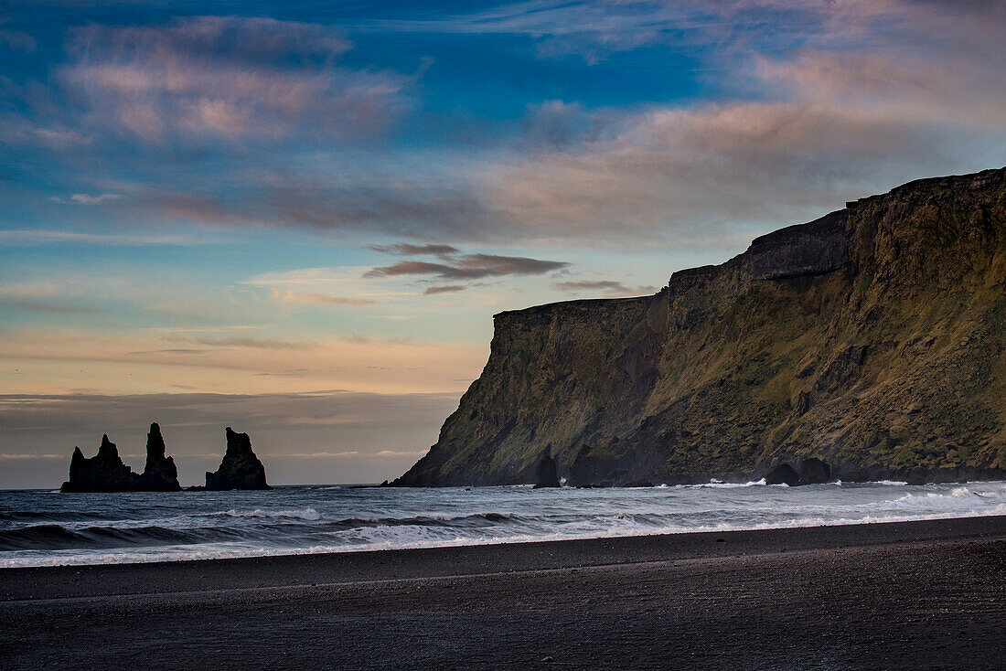 Blick auf Klippen und schwarzen Strand, Reynisfjara Beach, an der Südküste Islands, nahe der Stadt Vik, in der Dämmerung; Island