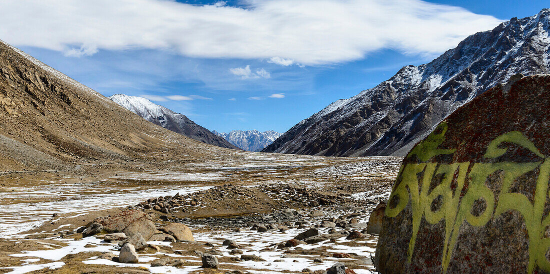 Eisiges Tal mit auf Felsen gemaltem Mantra und schneebedeckten Bergen dahinter in den Ausläufern des Himalaya in der Region Ladakh; Jammu und Kaschmir, Indien
