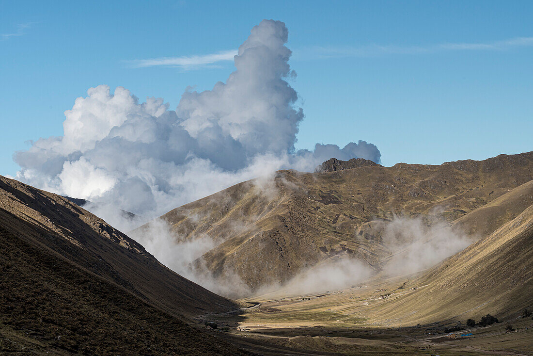 Wolken bilden sich am blauen Himmel über dem Dampf der heißen Quellen an den Berghängen im Lares-Tal; Cusco, Peru ; Lares-Tal, Cusco, Peru