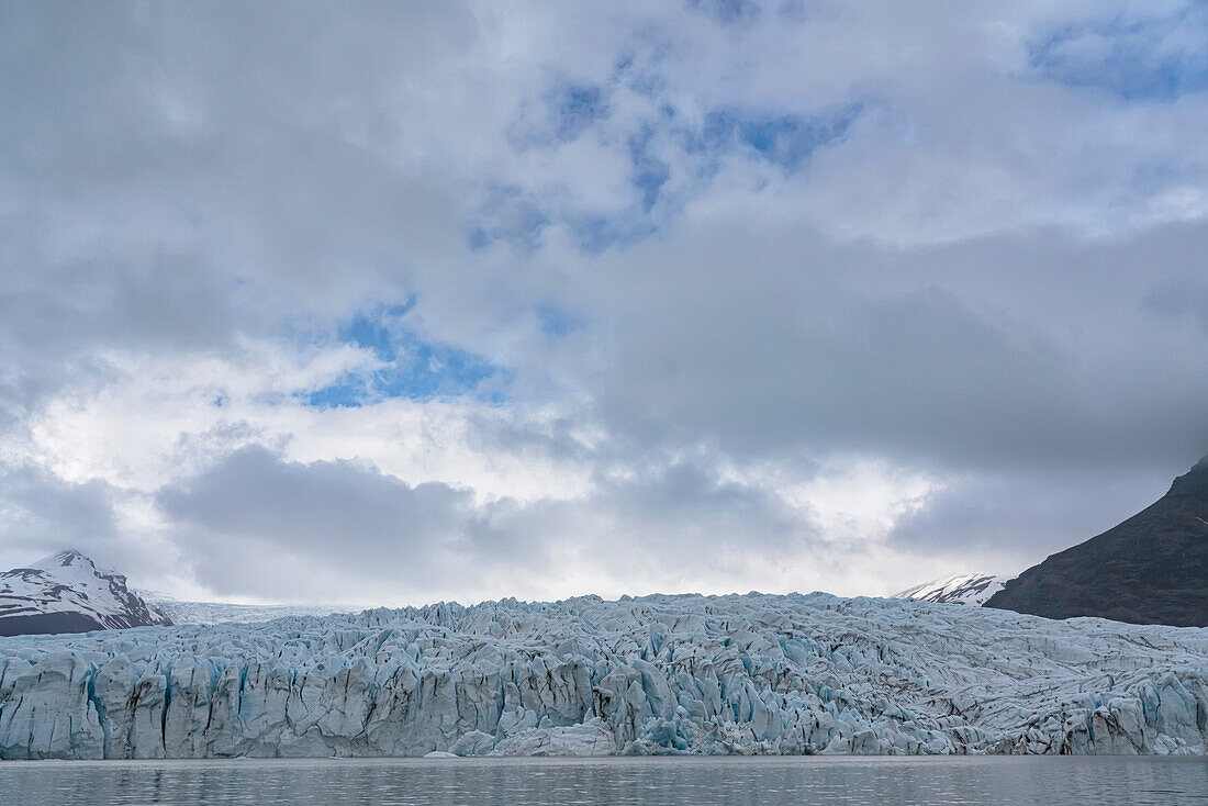 Blick von der Fjallsarlon Glacier Lagoon auf das blaue Eis des Fjallsjokull Glacier Terminus, das sich von den grauen Wolken abhebt, die den blauen Himmel bedecken, am südlichen Ende des berühmten isländischen Gletschers Vatnaj?l in Südisland; Südisland, Island