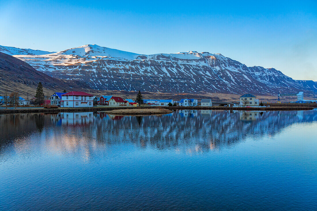 Scenic view of the town of Seyðisfjörður (Seydisfjordur) reflected in the clear, blue water; East Fjords, East Iceland, Iceland