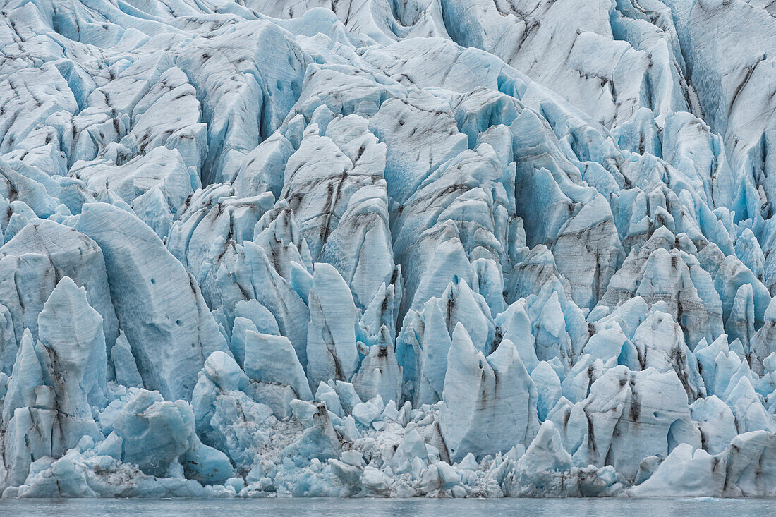 Stunning view of the silt streaked, jagged blue ice shapes of a glacier terminus; South Iceland, Iceland