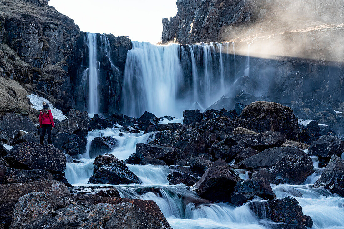 Frau steht in der Nähe eines Wasserfalls außerhalb von Sey?j?r in den Ostfjorden von Island; Ostisland, Island