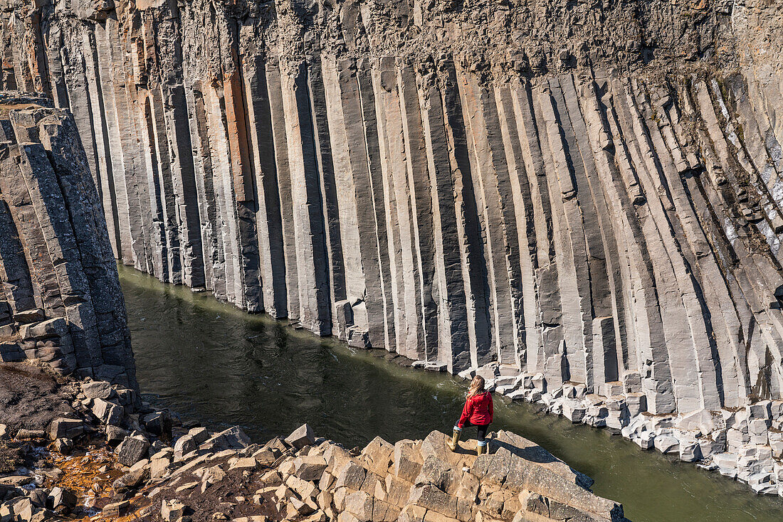 Frau steht am Rande einer felsigen Klippe und schaut auf die Basaltsäulen der Stu?il-Schlucht im Nordosten Islands, die eine erstaunliche und surreale Landschaft bilden; Stu?il-Schlucht, Nordisland, Island