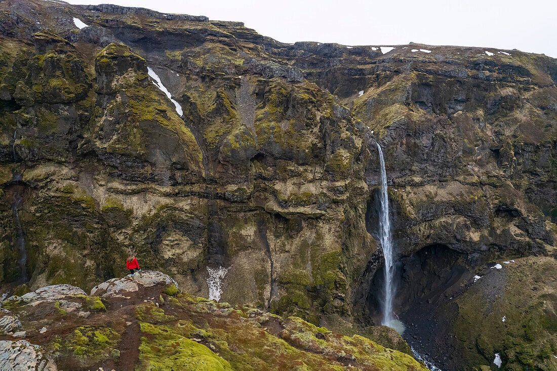 Frau steht mit Blick auf den Mulagljufur Canyon, ein Wanderparadies, und genießt die Aussicht auf einen Wasserfall und die moosbewachsenen Klippen; Vik, Südisland, Island