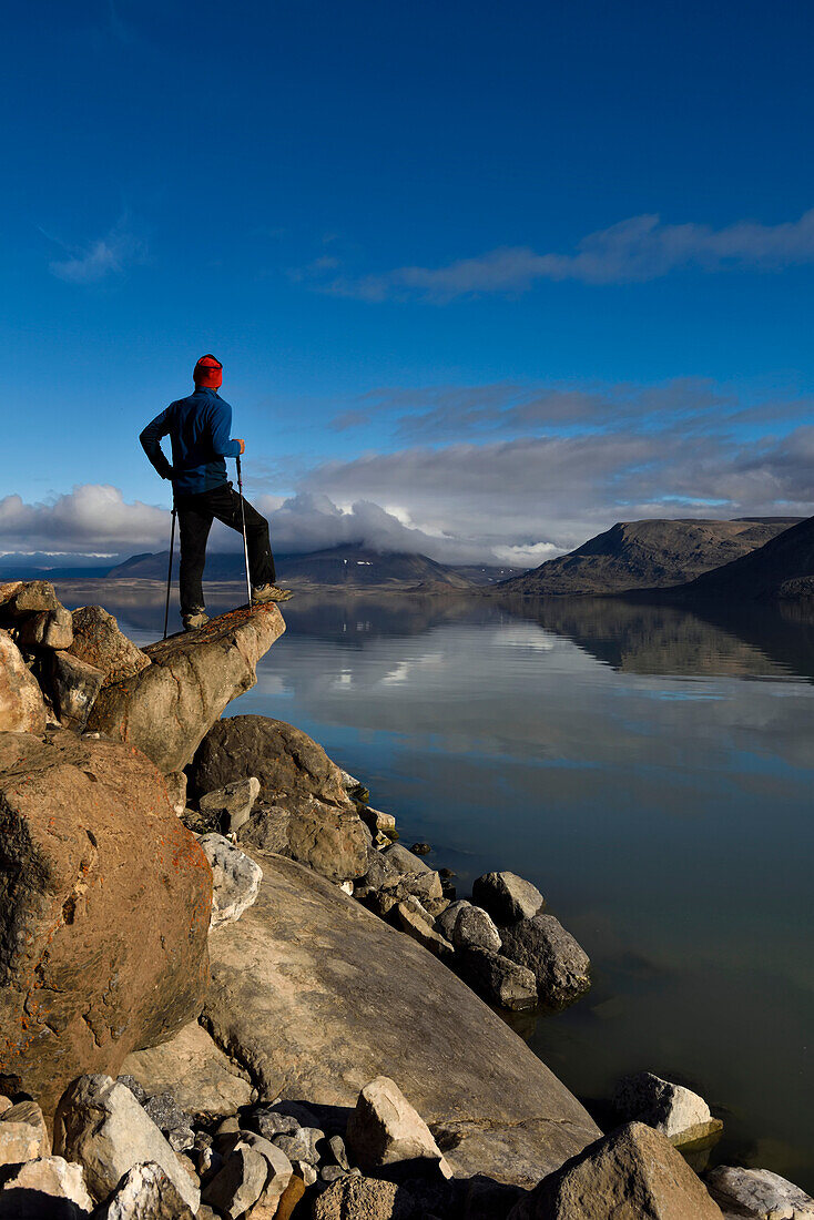 Ein Mitglied des Expeditionsteams steht auf einem großen Felsen und blickt auf den See Centrum. Die Spiegelungen der entfernten Berge sind fast so perfekt wie die Berge selbst.
