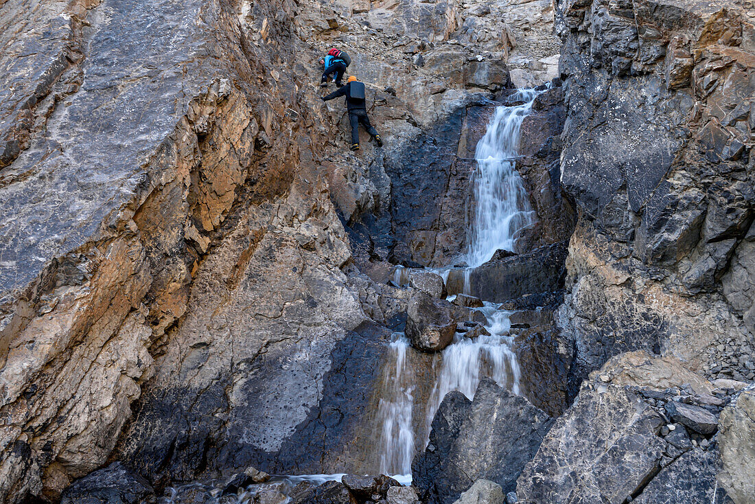 Expedition team member helps another descend a steep climb next to a very cold waterfall. One slip here. There's no rescue for days as the weather is too bad elswhere...