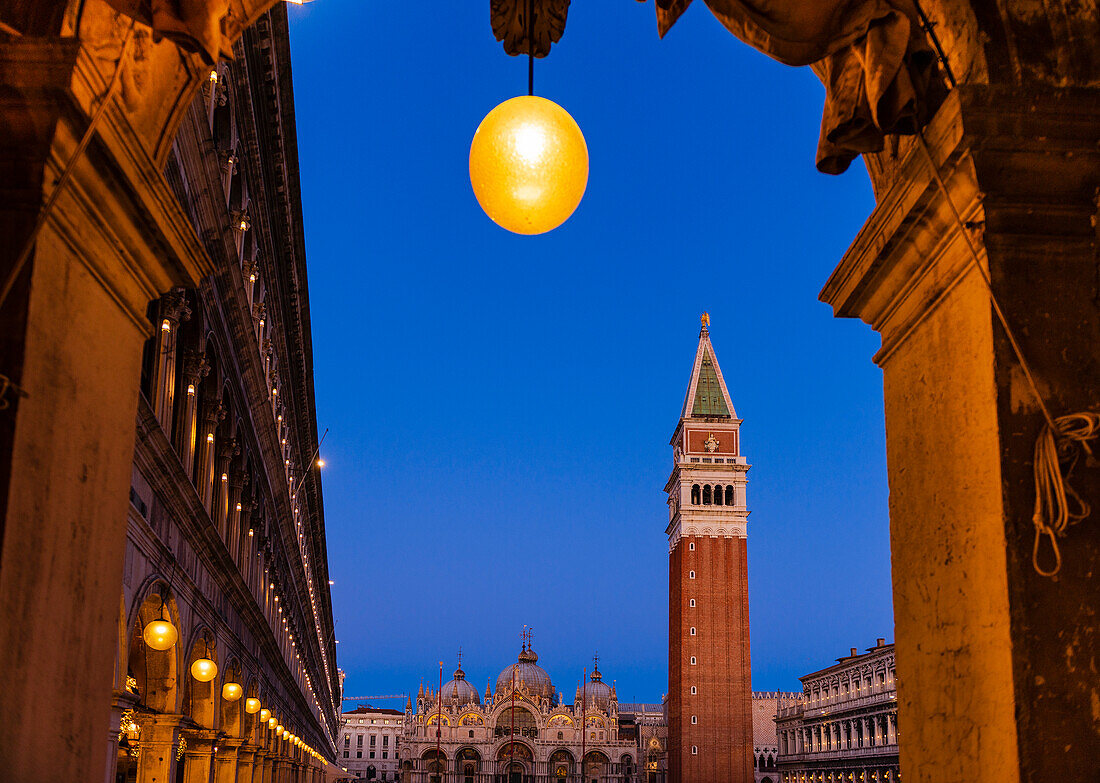 View of St Mark's Campanile and St Mark's Cathedral with lights illuminating the  Piazza San Marco in Veneto at dusk; Venice, Italy