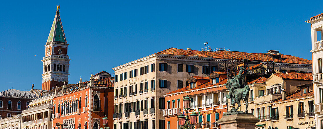 Dächer historischer Gebäude entlang der Uferpromenade Riva degli Schiavoni mit der Statue und dem Denkmal von Viktor Emanuel II. und der Turmspitze des Glockenturms von St. Markus; Venetien, Venedig, Italien