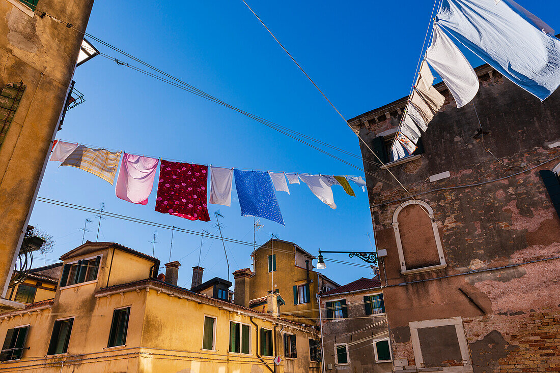 Hausdächer mit zum Trocknen aufgehängter Wäsche vor blauem Himmel im Stadtteil Castello; Venetien, Venedig, Italien