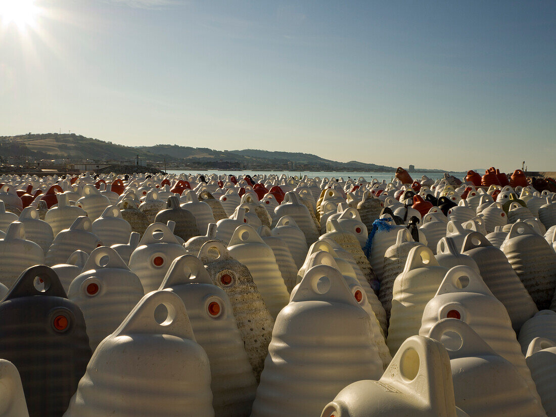 View of large quantity of floats used for mussel cultures on the shore in the late afternoon light with hills in the background; Porto San Giorgio, Marche, Italy