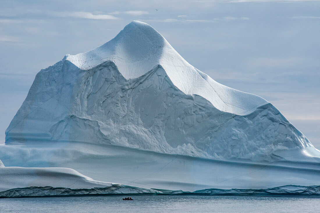 Reisende in einem Ausflugsboot fahren vor einem massiven, gewölbten Eisberg in der Antarktischen Straße in Grönland vorbei; Ostgrönland, Grönland