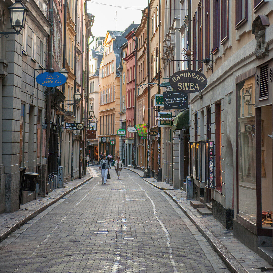 Fußgänger, die eine Straße mit an den Seiten der Gebäude angebrachten Ladenschildern entlanggehen; Stockholm Schweden