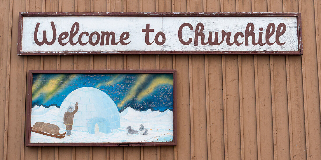Ein Gemälde und ein Schild an der Seite eines Gebäudes mit der Aufschrift "Willkommen in Churchill"; Churchill Manitoba Kanada