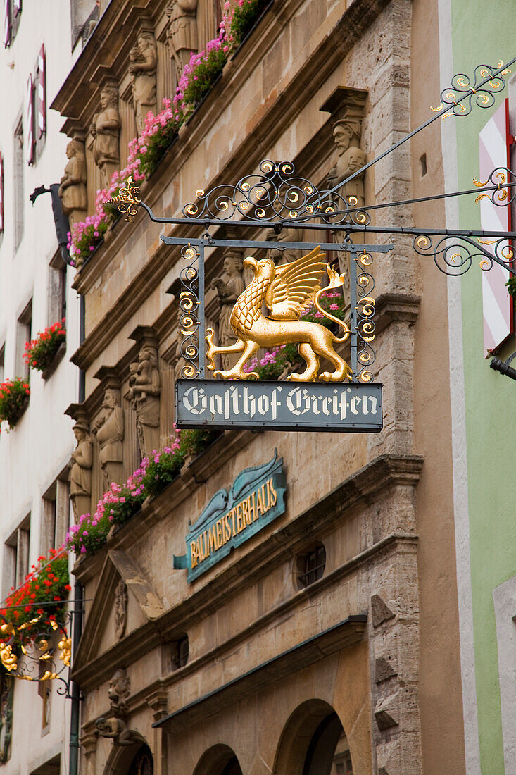 Sign Hanging From A Building With Blossoming Flowers In Window Planter Boxes; Rothenburg Ob Der Tauber Bavaria Germany