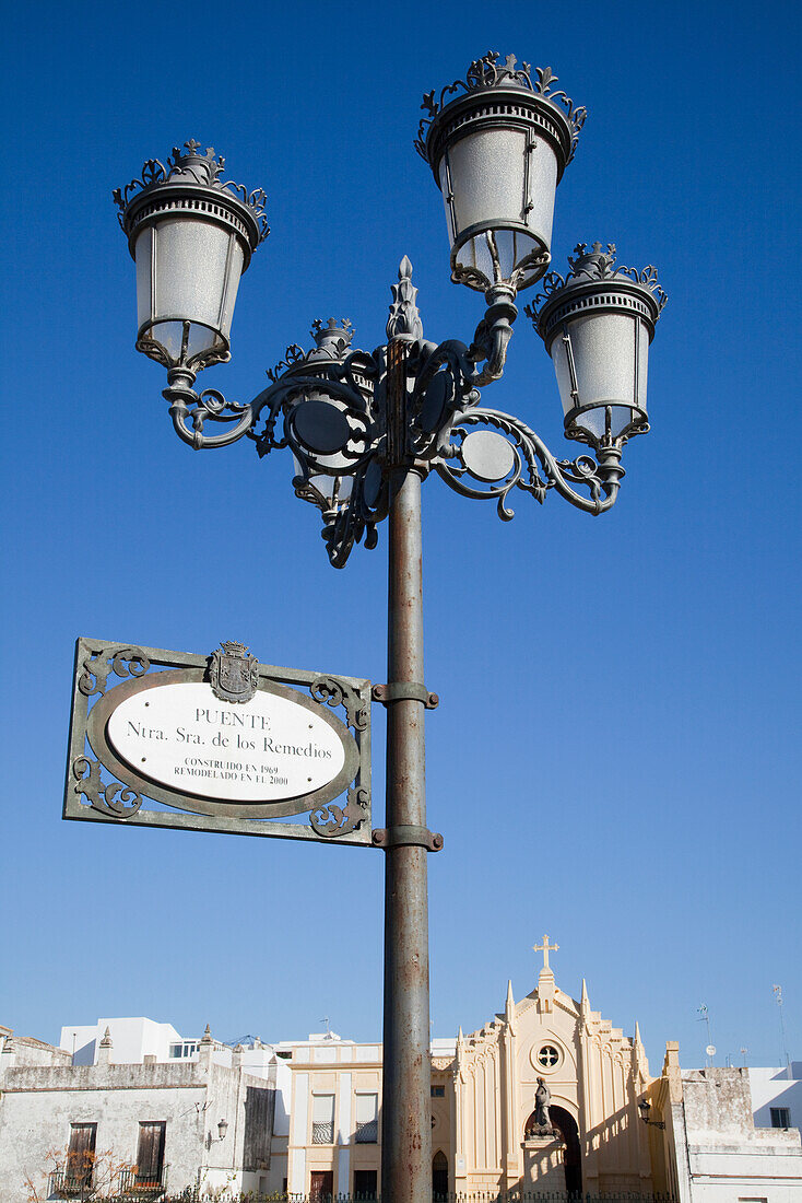 A Sign On A Lamp Post With A Church In The Background; Chiclana De La Frontera Andalusia Spai