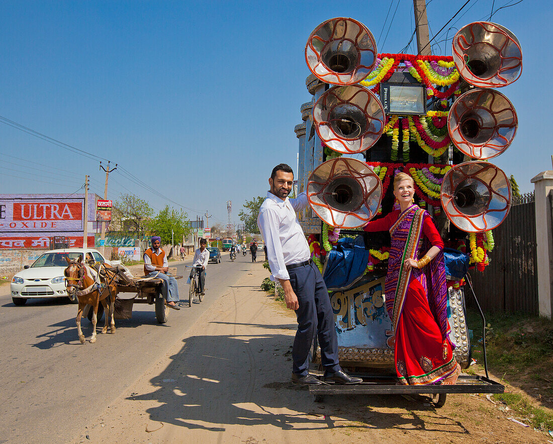 Ein gemischtrassiges Paar steht auf der Rückseite eines geschmückten Wagens am Straßenrand; Ludhiana, Punjab, Indien