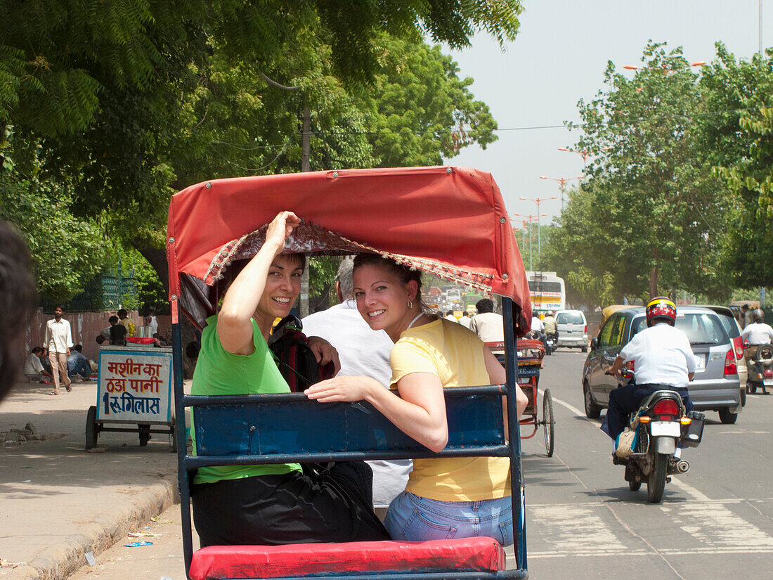 Zwei Mädchen reiten eine Rikscha auf einer belebten Straße; Delhi Uttar Pradesh Indien