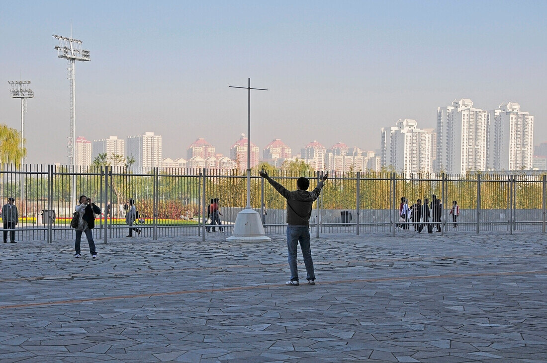 A Tourist Stands Posing For A Photograph With Arms Raised; Beijing China