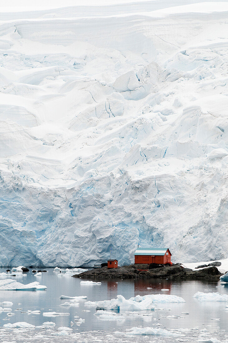 Kleine Gebäude spiegeln sich im Wasser an der gefrorenen Küste; Antarktis