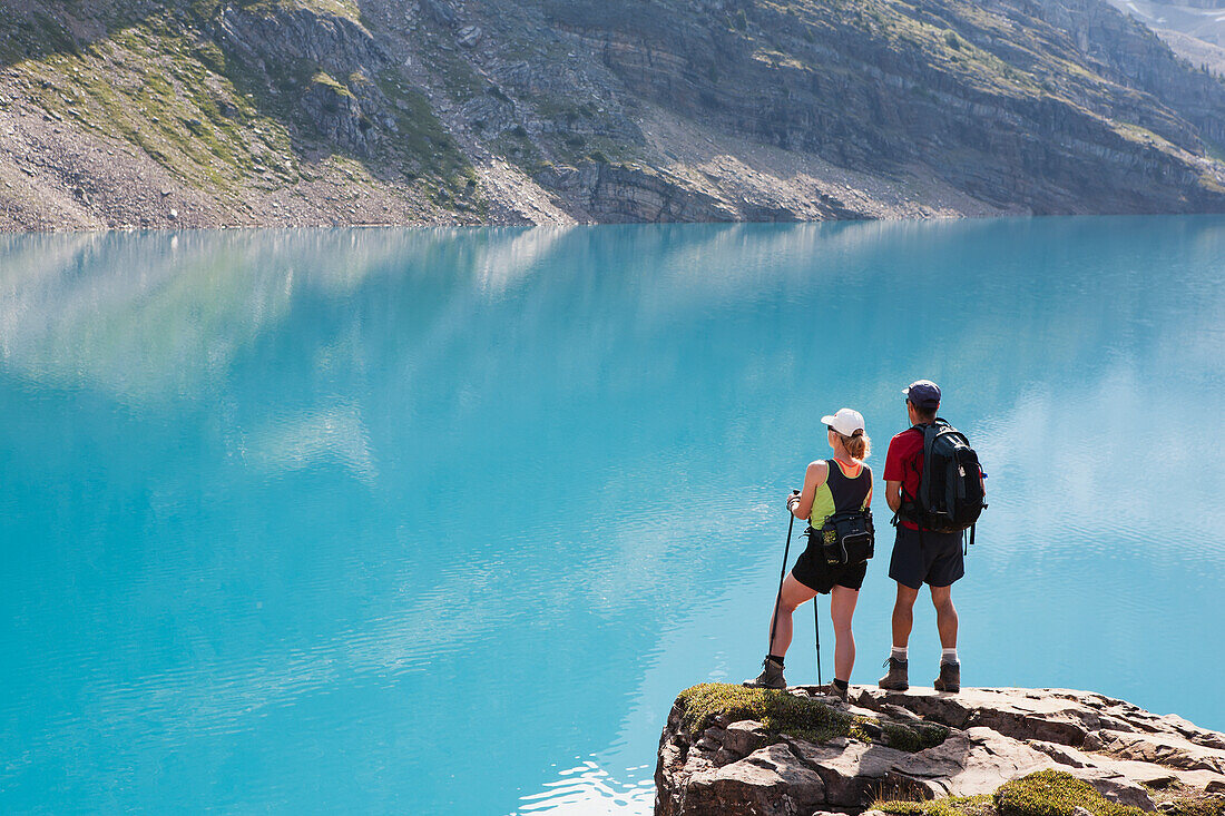 Female And Male Hikers On Rock Cliff Overlooking Mountain Lake; Field British Columbia Canada