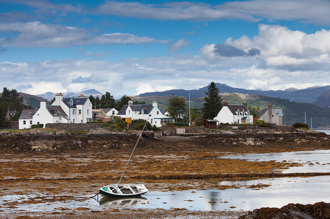 Ein Boot liegt bei Ebbe am Ufer mit Häusern entlang der Küste; Plockton Highlands Schottland