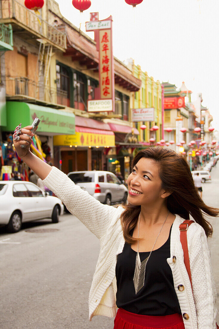 A woman takes a picture of herself with her cell phone camera in a busy urban area; san francisco california united states of america