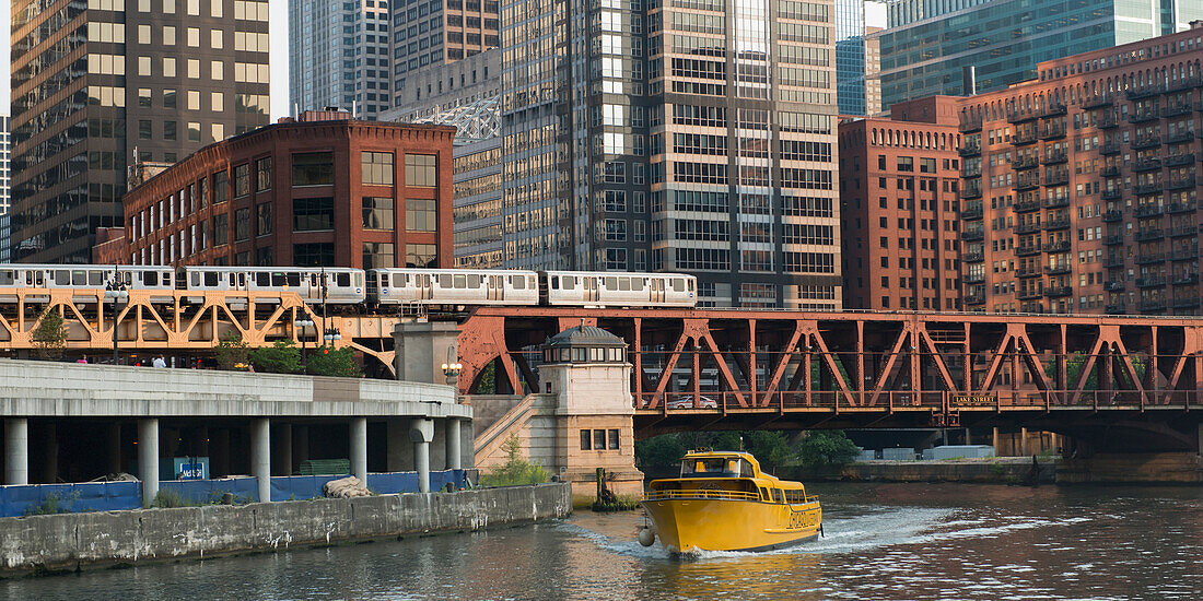 Ein gelbes Boot auf dem Fluss, das unter einer Brücke hindurchfährt, mit dem Zug und Gebäuden im Hintergrund; Chicago Illinois Vereinigte Staaten von Amerika