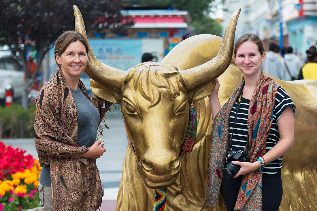 Zwei Touristinnen posieren neben der Statue einer goldenen Kuh; Lhasa, Xizang, China