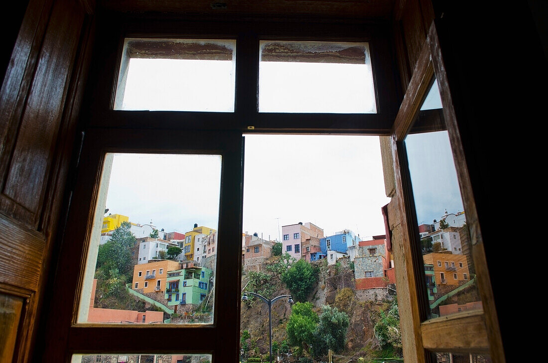 Mexiko, Bundesstaat Guanajuato, Guanajuato, Blick durch ein altes Holzfenster auf eine Hangszene mit alten spanischen Häusern