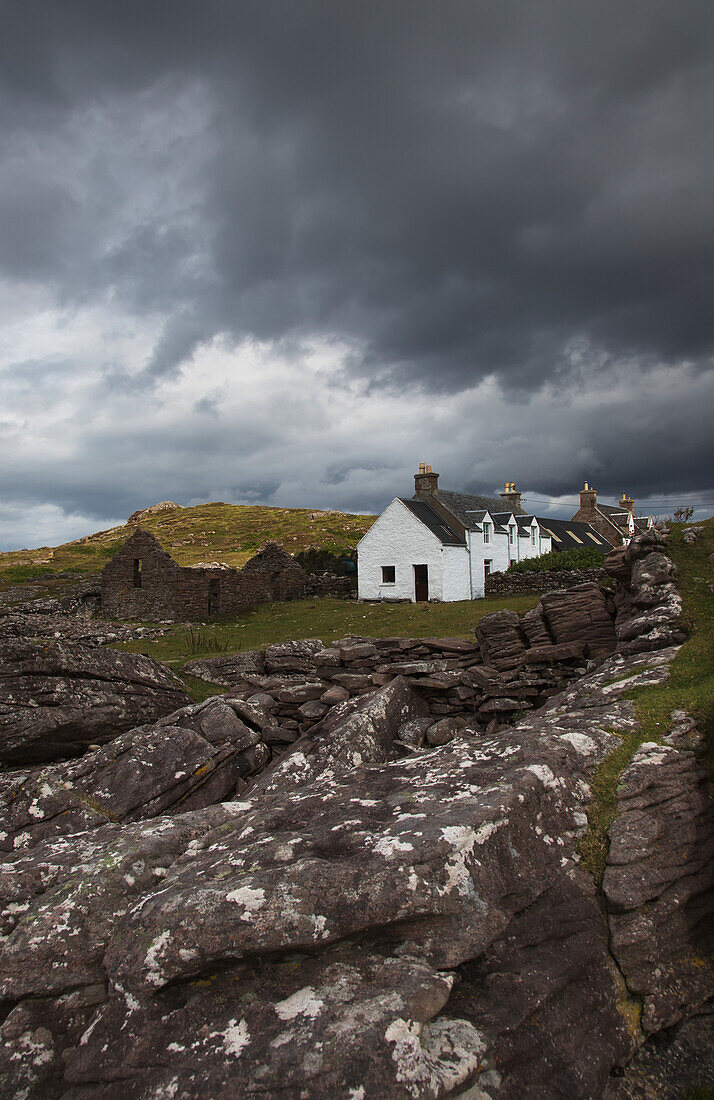 UK, Schottland, Highlands, Applecross Peninsula, Steinmauer und Cottage-Häuser unter stürmischem Himmel