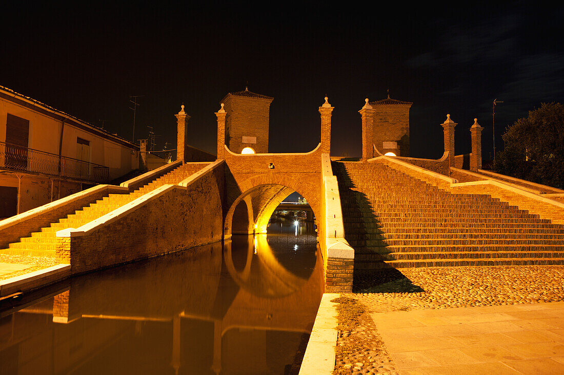 Steinbrücke mit Türmen und Stufen, die sich im Wasser spiegeln, Nacht; Comacchio, Emilia-Romagna, Italien