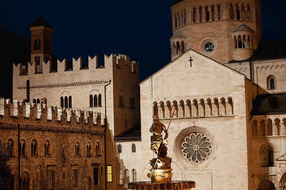 Italy, Trentino, Trento, Cathedral square, Illuminated Neptune fountain at night and stone walls of cathedral and palace in background