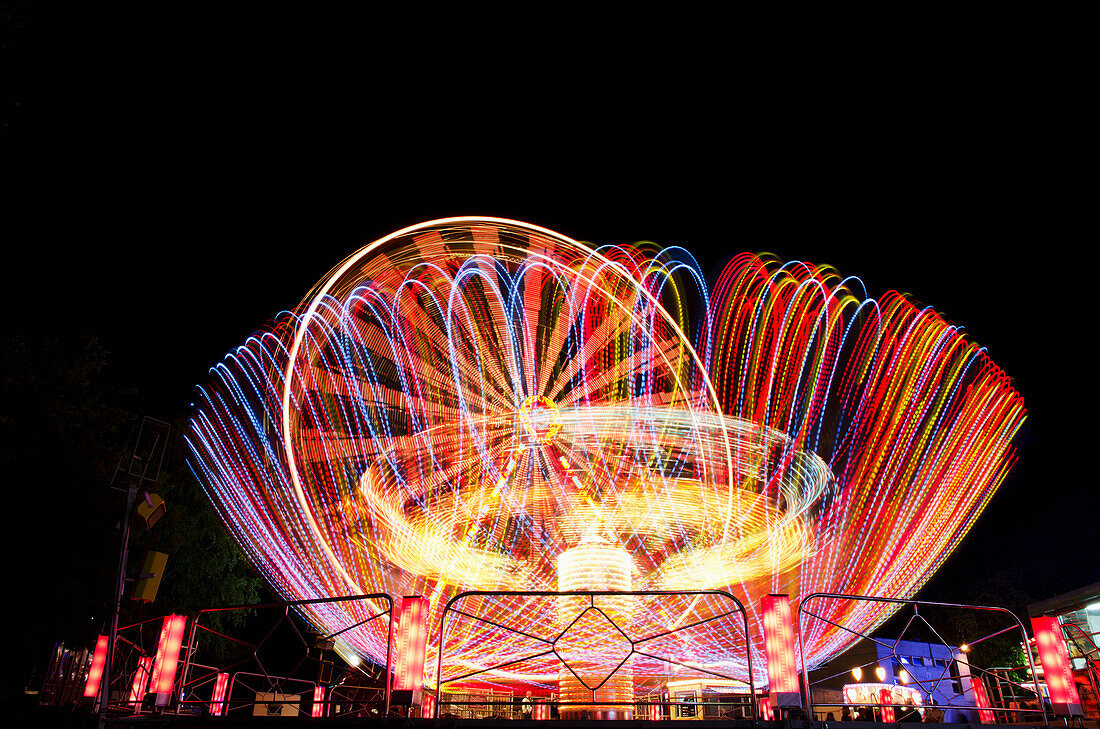 Bunte Lichter verschwimmen auf nächtlichen Vergnügungspark-Fahrgeschäften; Locarno, Tessin, Schweiz