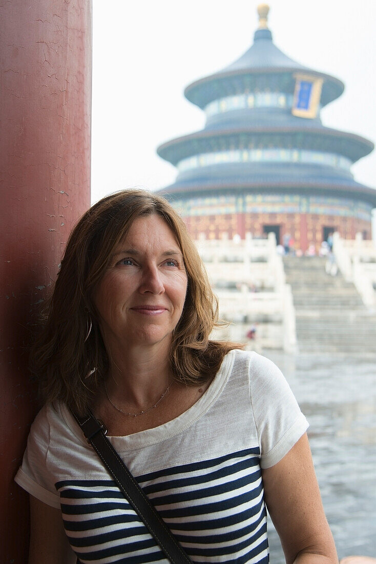 A Woman Leans On A Wall With The Temple Of Heaven In The Background; Beijing, China