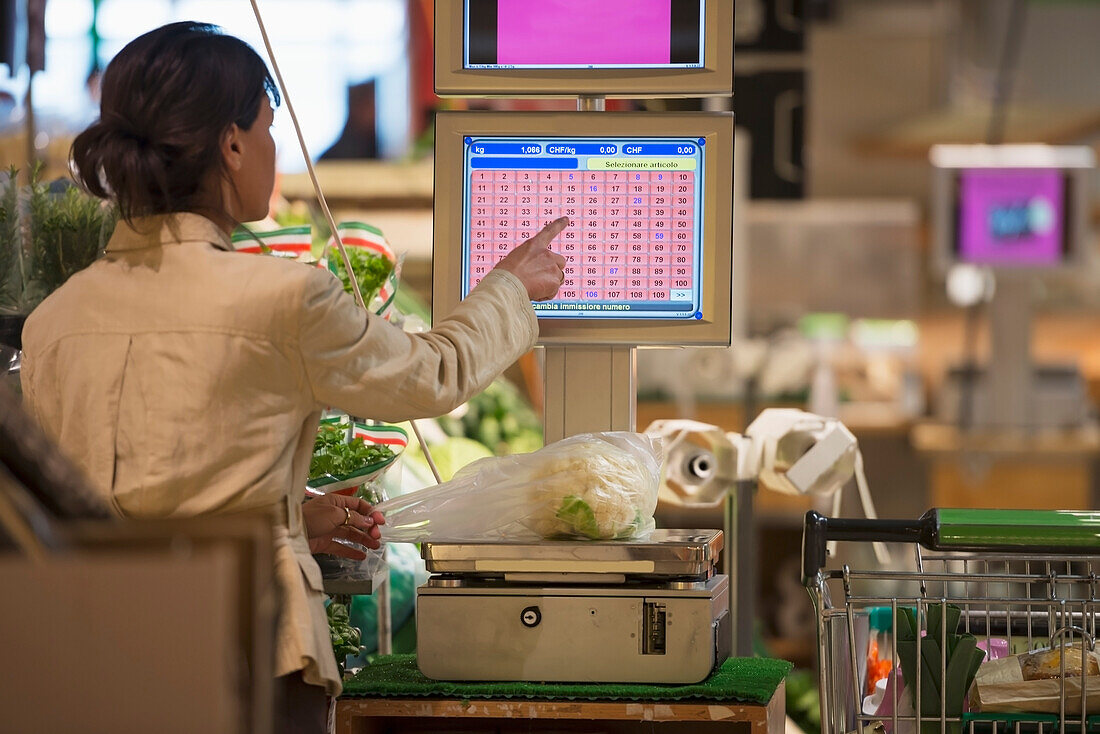 A Cashier Weighs Fresh Produce On A Scale And Chooses A Button On The Screen At Checkout; Ascona, Ticino, Switzerland