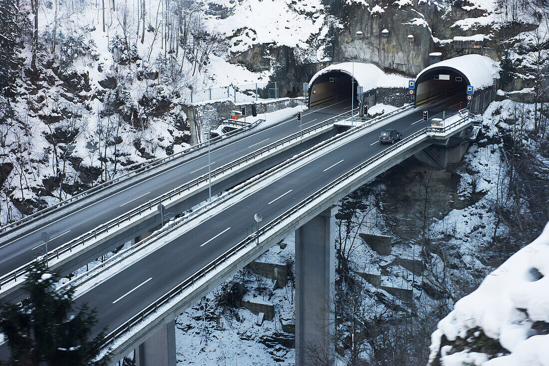 Straßen und Tunnel, die nebeneinander in einen Berghang hinein und aus ihm heraus führen; Uri, Schweiz
